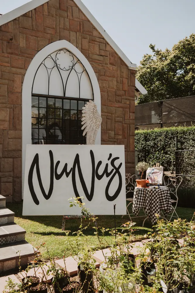 The Nunu's sign in a stone arch, with tables on the lawn